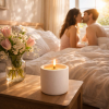 Lit candle in a minimalist white concrete jar on a bedside table with flowers, sunlight streaming through a window and a couple softly embracing in the background.
