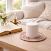 White concrete candle resting on a hand-crocheted cotton mat on a light wooden table in a bright, airy living room.